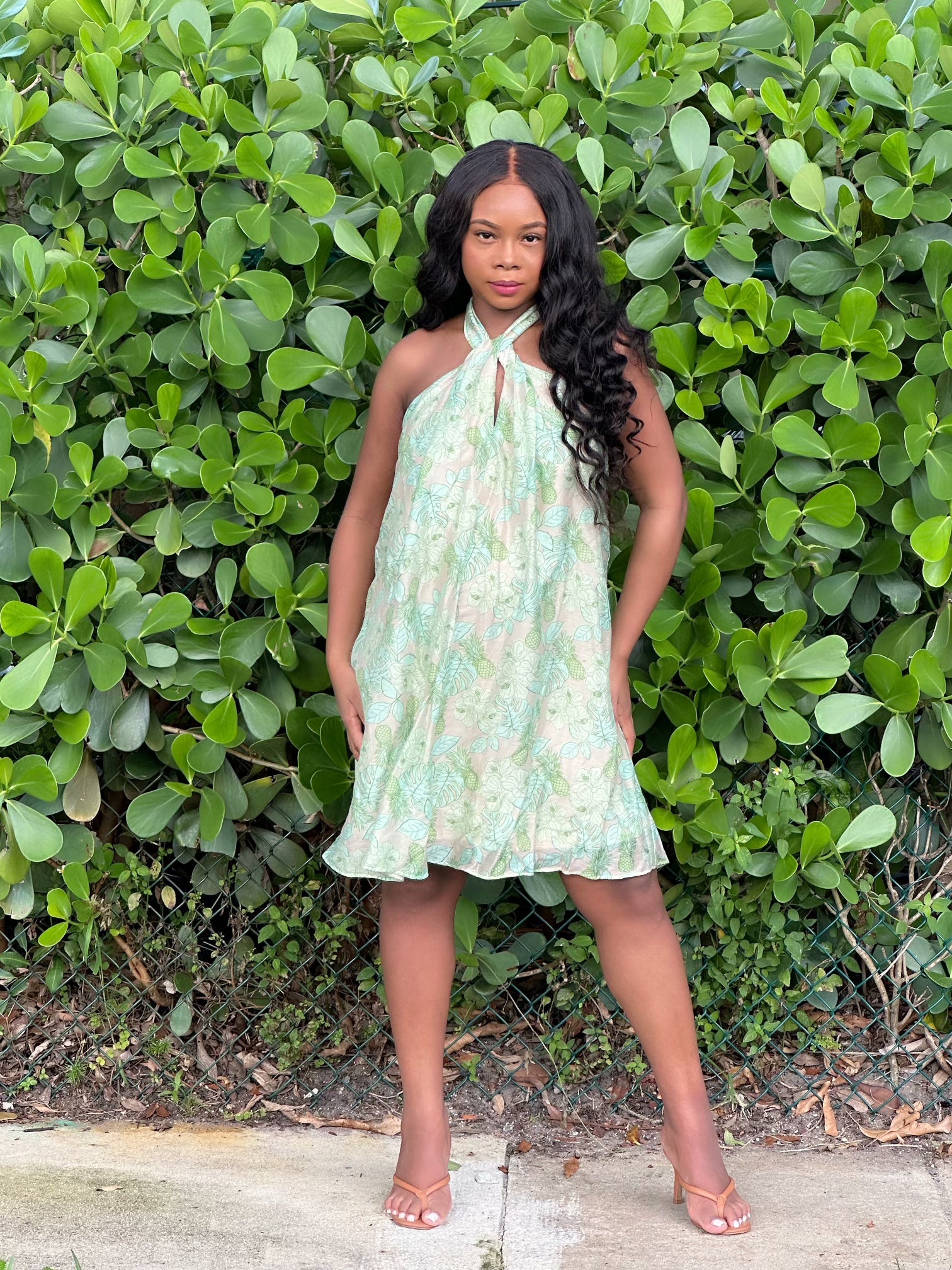 Au Natural Dress in a halter top style with vibrant green and pink floral print, modeled outdoors against lush greenery. Perfect mini dress for summer outings.